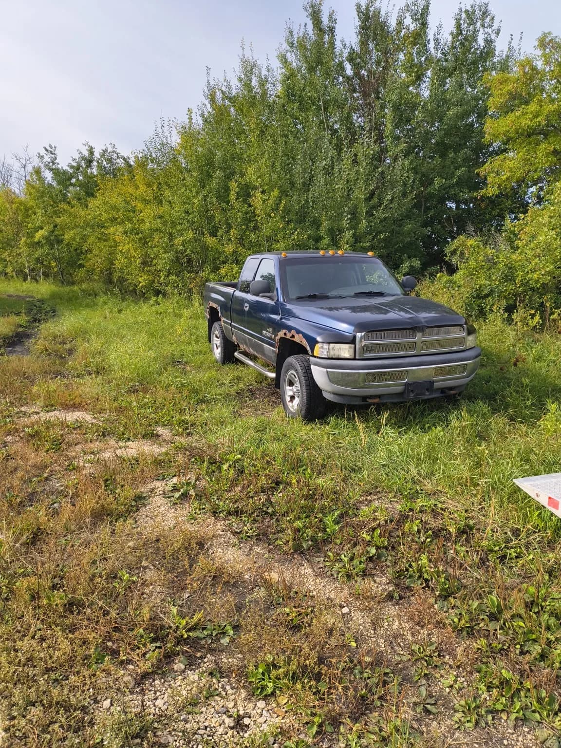 Older blue Dodge pickup with rust parked on a rural Manitoba property