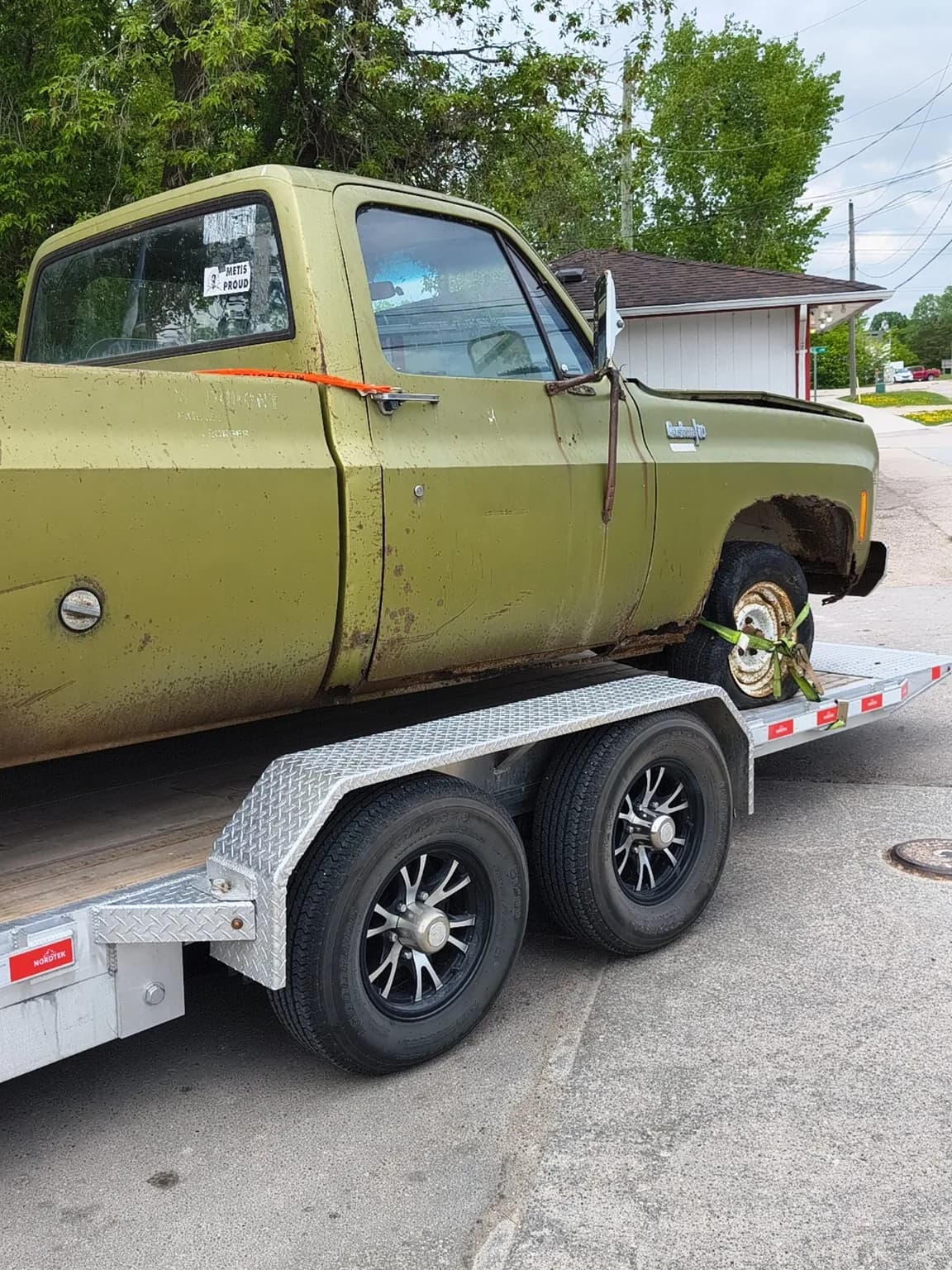 Old green Chevrolet pickup with visible rust secured on a trailer