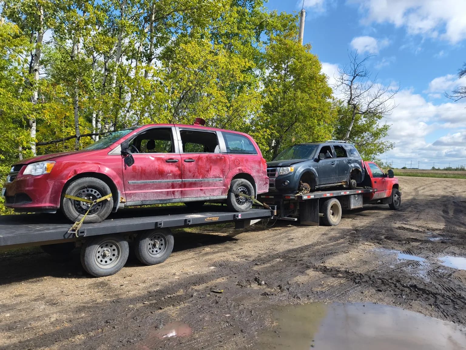 Recycle Your Ride hauling a red minivan and grey SUV with two trucks in Manitoba